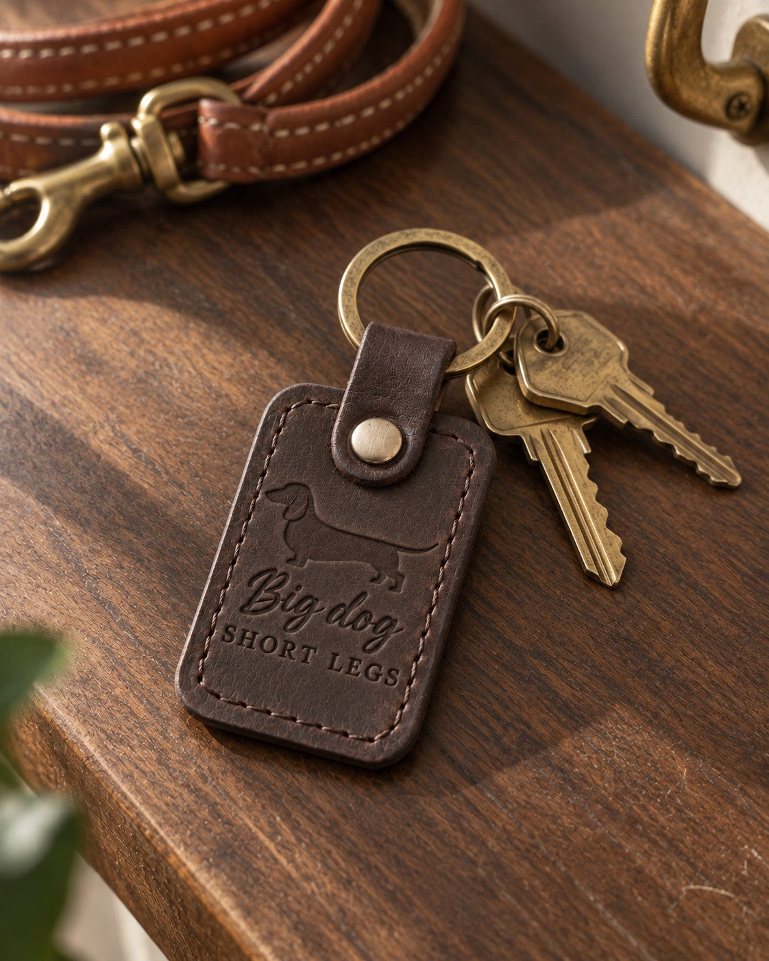 Dark brown Big Dog Short Legs keychain lying on a walnut table with brass keys and a leather leash behind