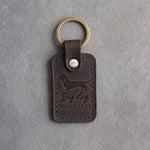 Dark espresso leather keychain debossed with a dachshund silhouette and the words Big dog SHORT LEGS, on gray concrete