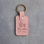 Blush pink leather keychain debossed with a large acorn beside a small acorn above Big sister and EST 2026