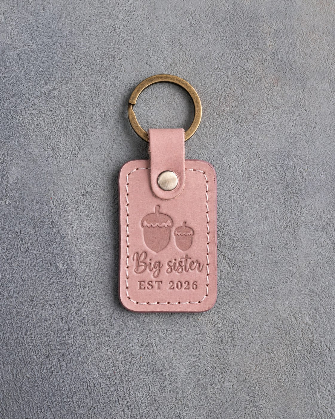 Blush pink leather keychain debossed with a large acorn beside a small acorn above Big sister and EST 2026