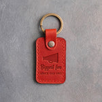 Poppy red leather keychain debossed with a megaphone and the words Biggest fan SINCE DAY ONE, on gray plaster