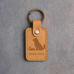 Indian Summer tan leather keychain debossed with a sitting dog beside a training bumper above BIRD DOG, on gray concrete