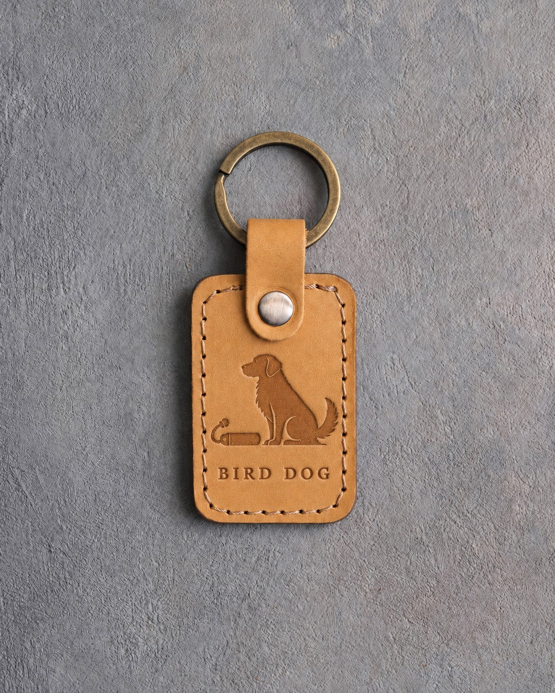 Indian Summer tan leather keychain debossed with a sitting dog beside a training bumper above BIRD DOG, on gray concrete