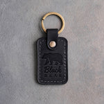 Black leather keychain debossed with a walking black bear above the words Black BEAR, on gray plaster
