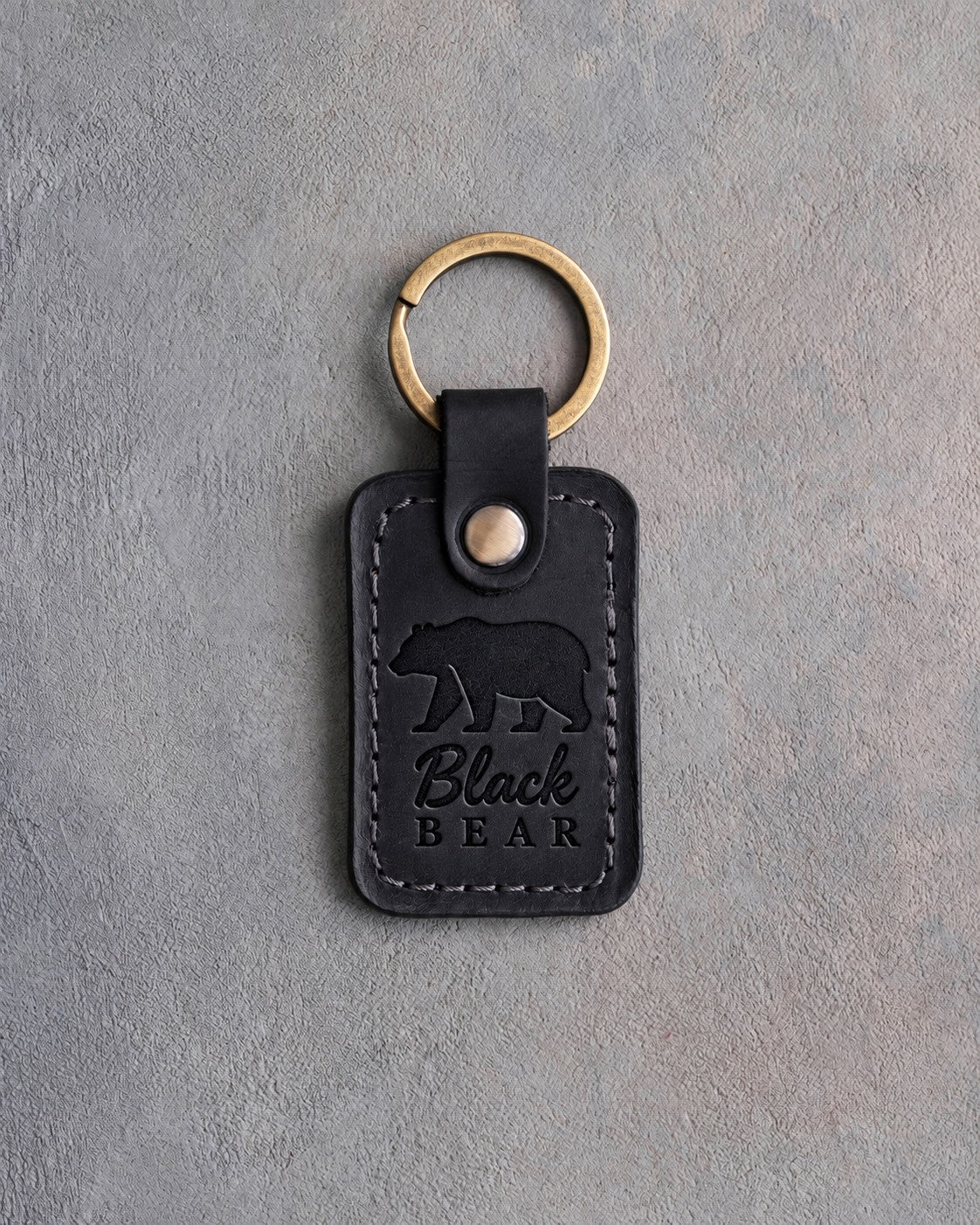 Black leather keychain debossed with a walking black bear above the words Black BEAR, on gray plaster
