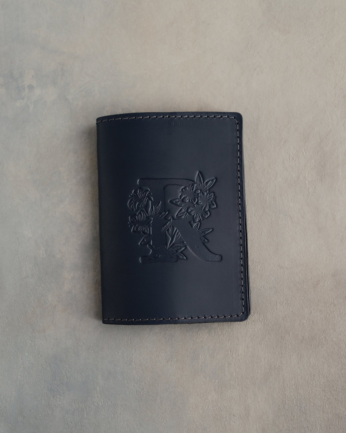 Black leather passport cover with a large floral initial pressed into the front