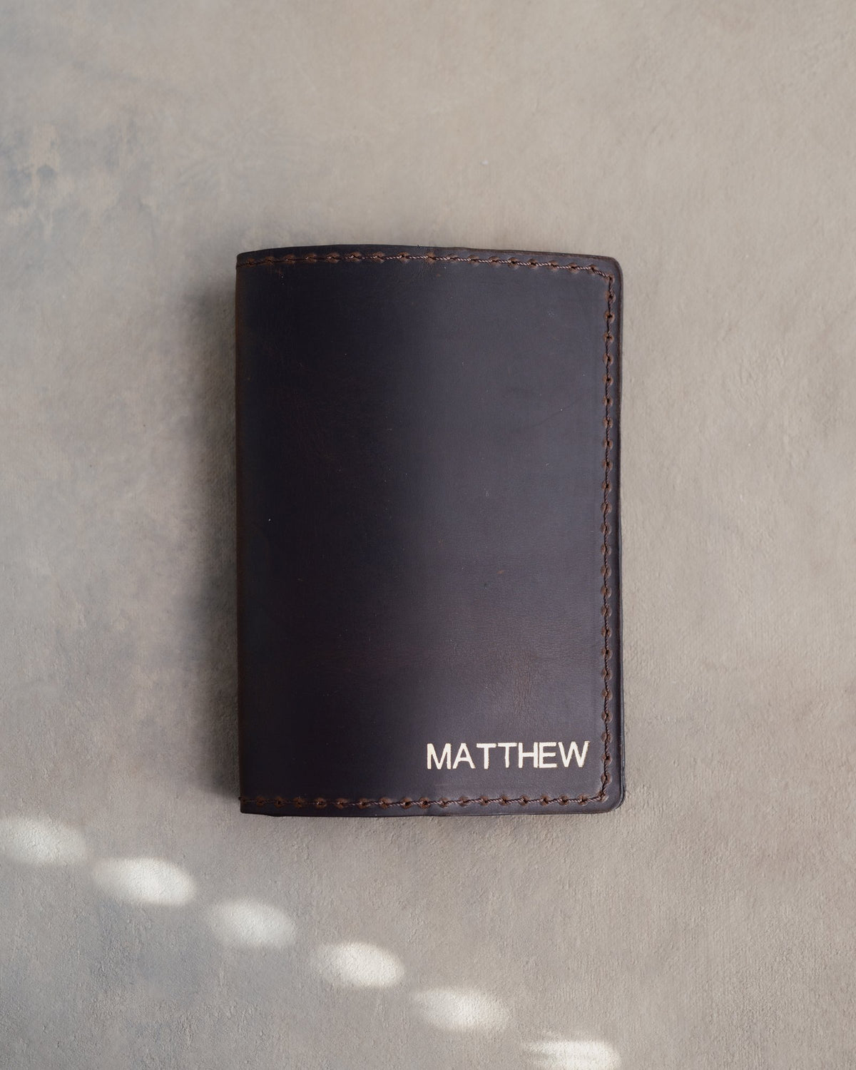 Black leather passport cover with the name MATTHEW in straight capitals in the bottom corner