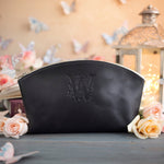 Black leather makeup bag with a floral monogram deboss, roses and a lit lantern in the background