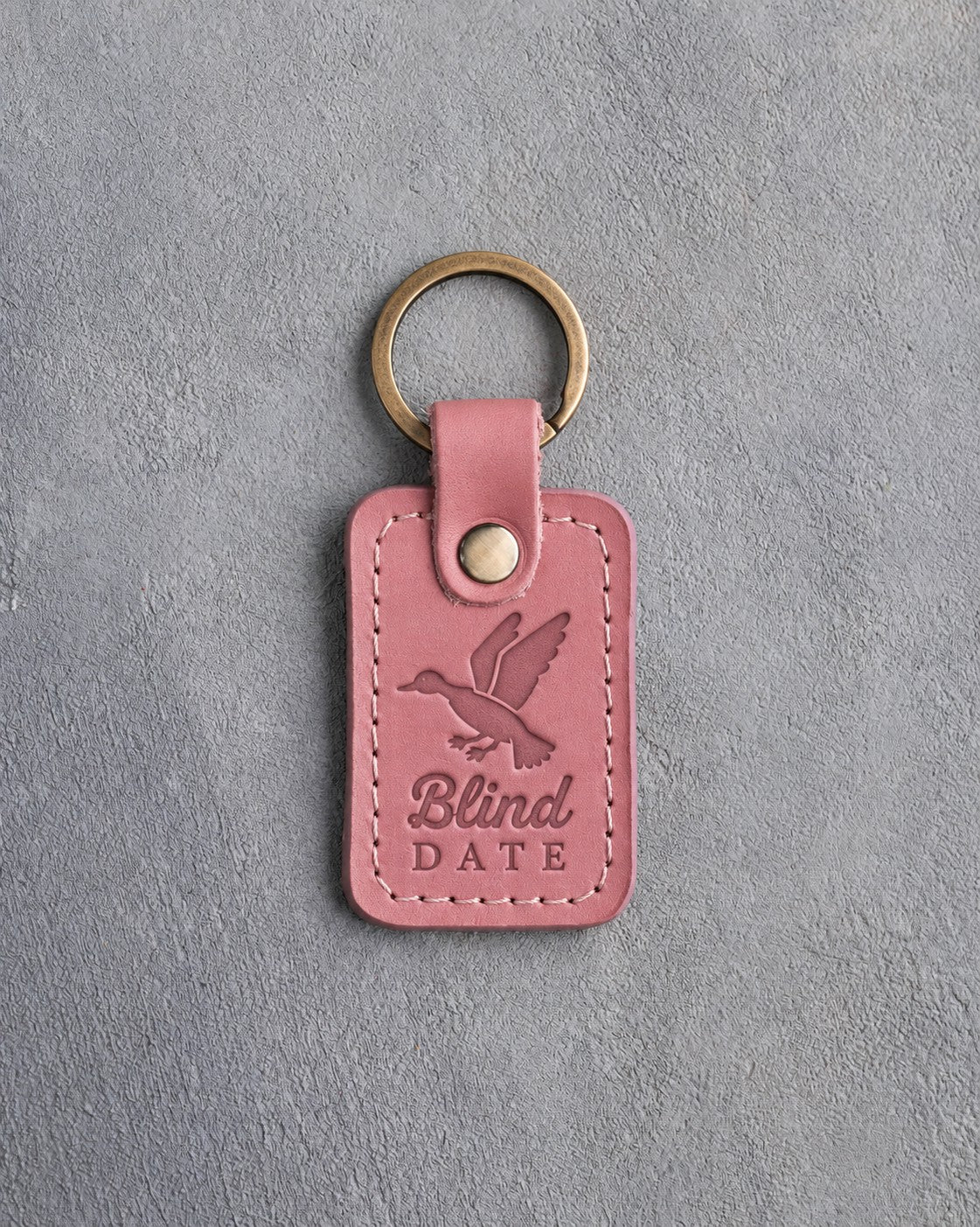 Rose pink leather keychain debossed with a mallard cupped to land above the words Blind DATE, on gray plaster