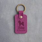 Fuchsia pink leather keychain debossed with a Bichon Frise and the words Blitz IN PROGRESS, on gray concrete