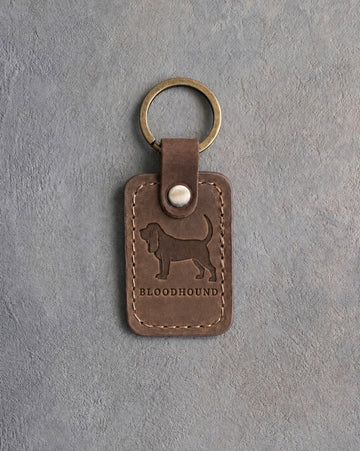 Sicilian brown leather keychain debossed with a Bloodhound silhouette above BLOODHOUND, on gray concrete