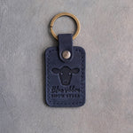 Blueberry navy leather keychain debossed with a front-facing steer above the words Blue ribbon SHOW STEER, on gray concrete