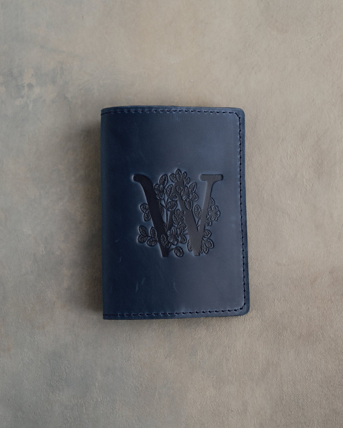 Blueberry leather passport cover with a large floral initial W pressed into the front