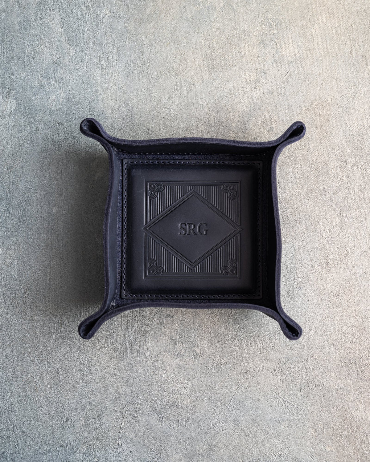 Blueberry leather valet tray with snapped corners and the initials SRG pressed into the diamond frame, seen from above