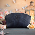 Blueberry navy initial makeup pouch with a floral monogram, staged among pale roses on a slate table