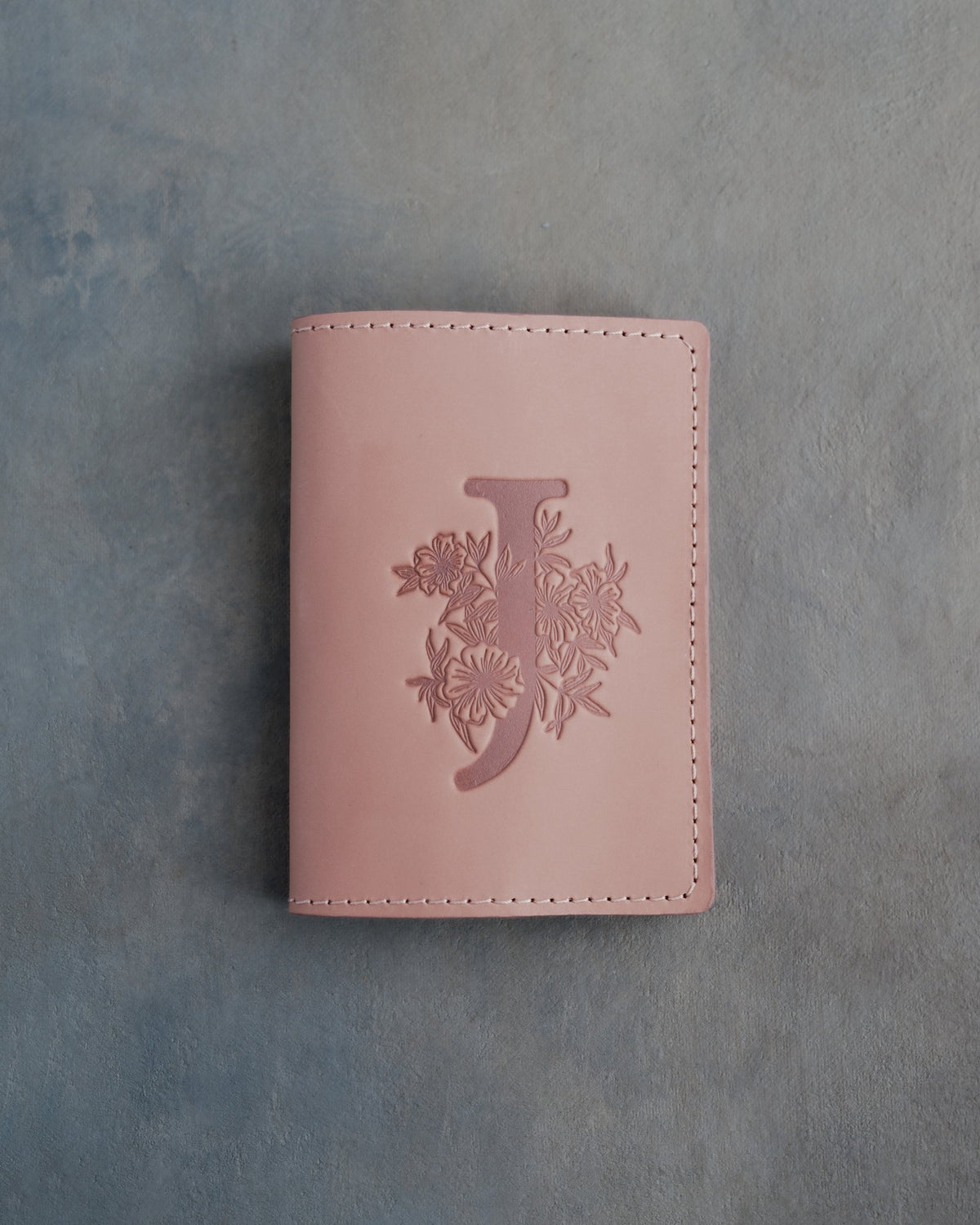 Blush leather passport cover with a large floral initial J pressed into the front