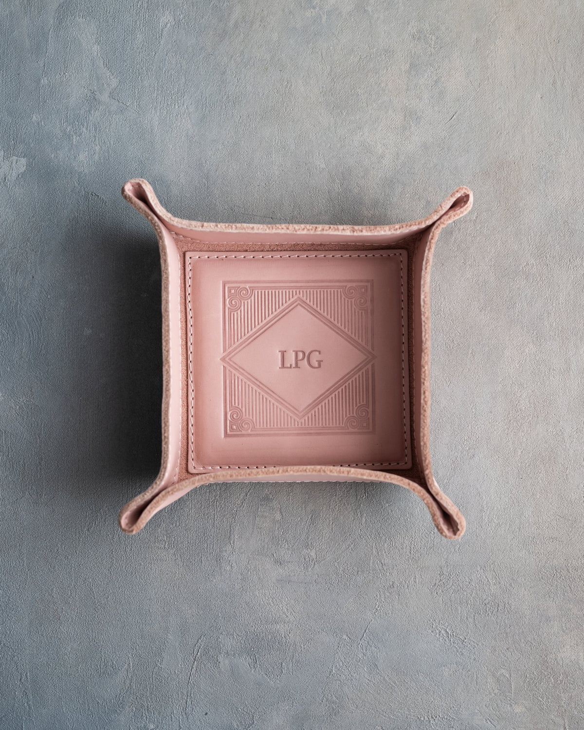 Blush leather valet tray with snapped corners and the initials LPG pressed into the diamond frame, seen from above