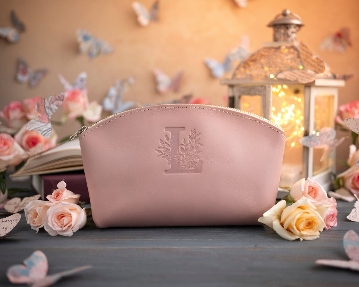 Blush pink leather makeup bag with a floral monogram deboss, roses and a lit lantern in the background