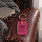 Bright pink Book BOYFRIEND keychain on a stack of romance paperbacks beside a mug