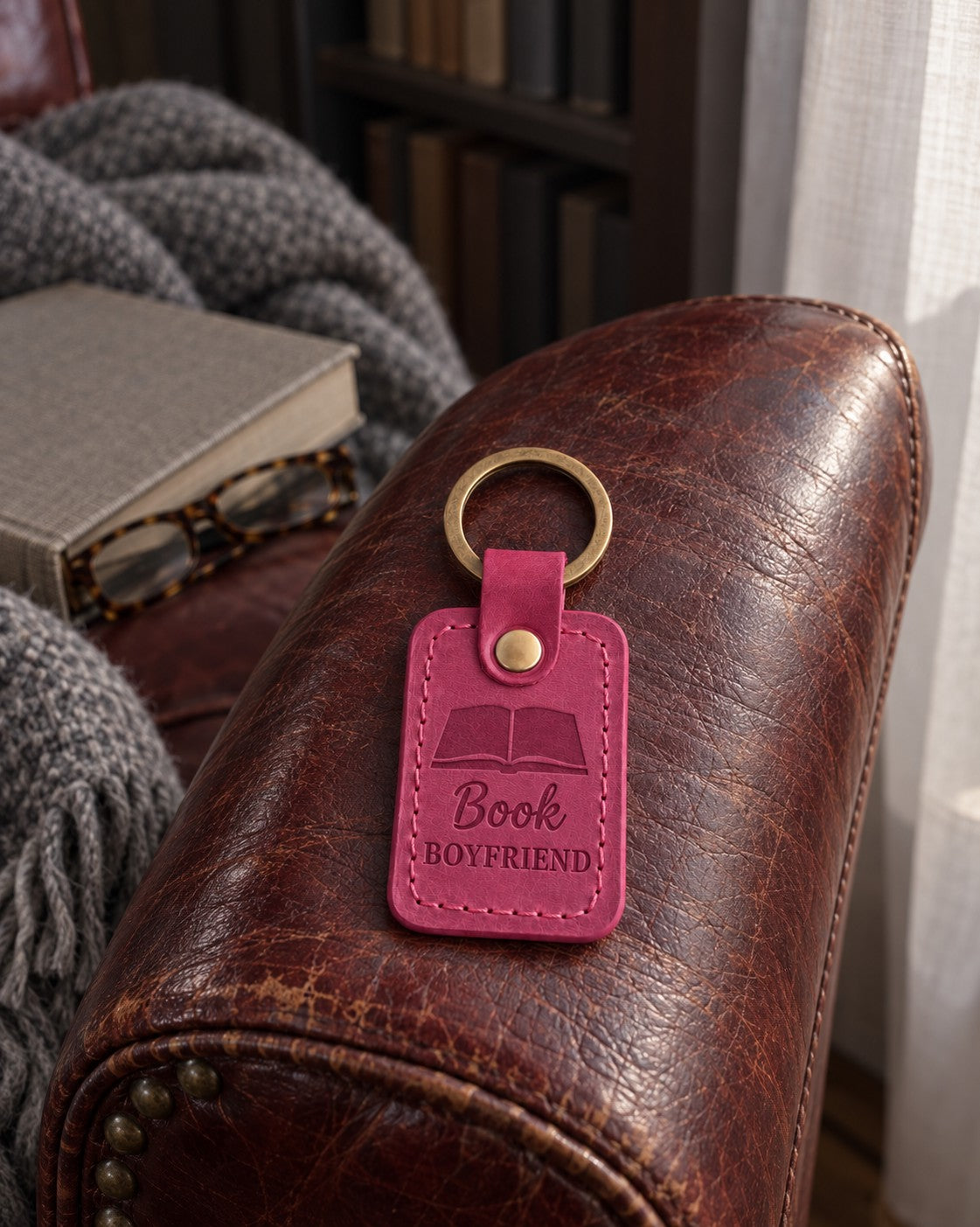 Bright pink Book BOYFRIEND keychain on a stack of romance paperbacks beside a mug
