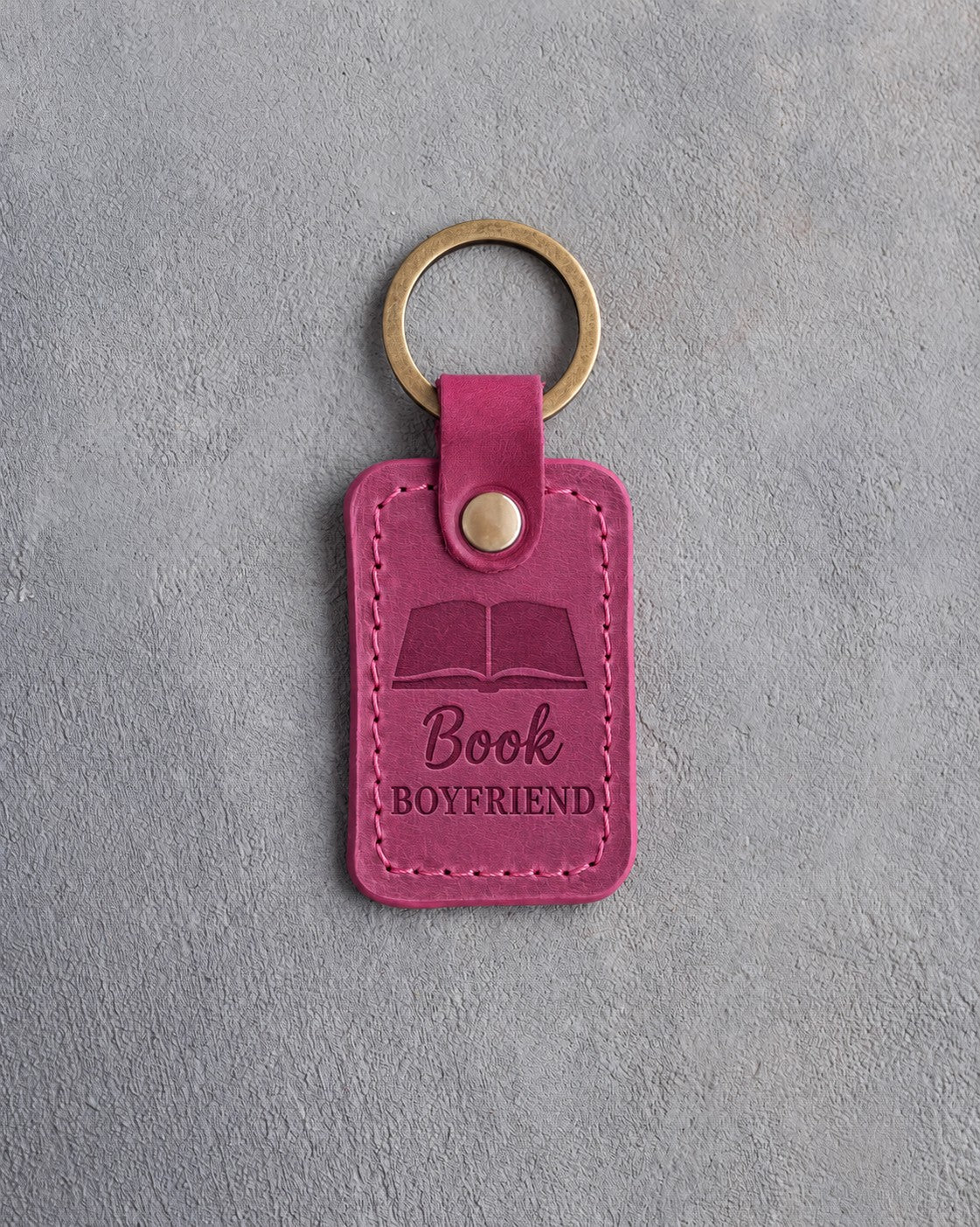 Fuchsia leather keychain debossed with an open book above Book and BOYFRIEND, on gray concrete