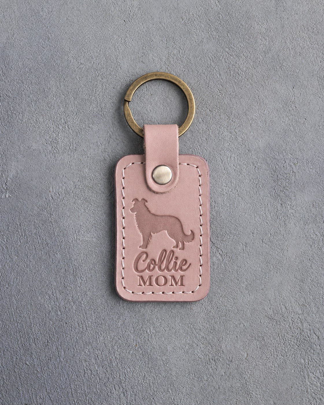 Blush pink leather keychain debossed with a border collie silhouette and Collie MOM lettering, on gray concrete