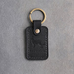 Black leather keychain debossed with a border collie above THE COLLIE, on gray concrete