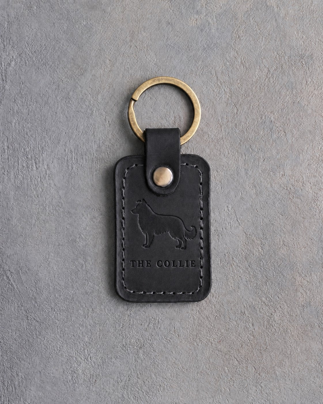 Black leather keychain debossed with a border collie above THE COLLIE, on gray concrete