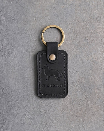 Black leather keychain debossed with a border collie above THE COLLIE, on gray concrete