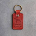 Poppy red leather keychain debossed with a Rhodesian Ridgeback silhouette and the words Born with A MOHAWK, on gray concrete