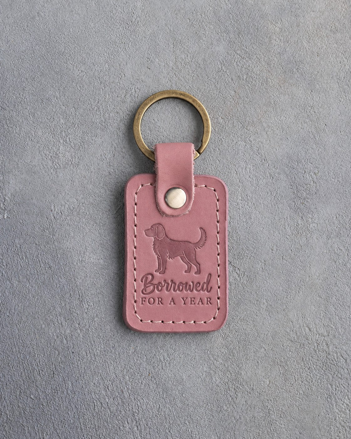 Parisian Blossom pink leather keychain debossed with a young puppy and the words Borrowed FOR A YEAR, on gray concrete
