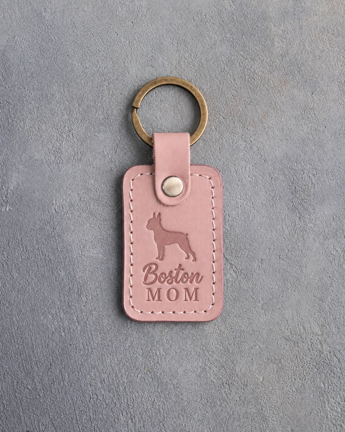 Blush pink leather keychain debossed with a Boston Terrier silhouette and the words Boston MOM, on gray concrete
