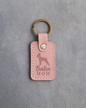 Blush pink leather keychain debossed with a Boston Terrier silhouette and the words Boston MOM, on gray concrete