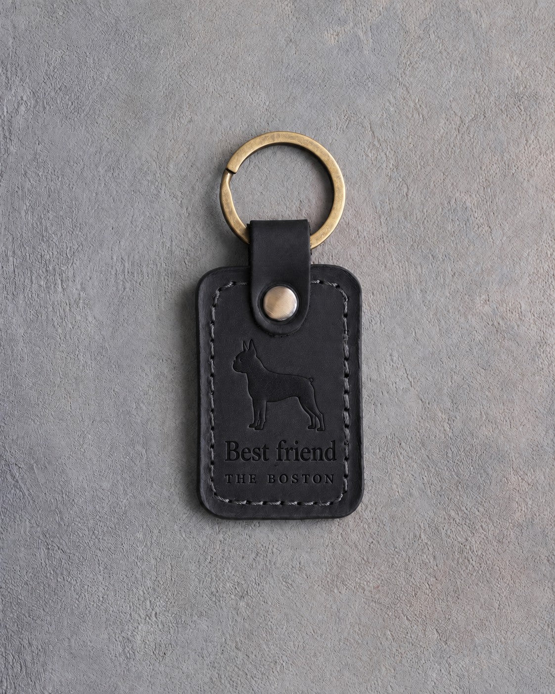 Black leather keychain debossed with a Boston Terrier silhouette above Best friend and THE BOSTON, on gray concrete