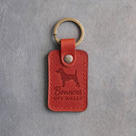 Poppy red leather keychain debossed with a Jack Russell terrier and the words Bounces OFF WALLS, on gray concrete