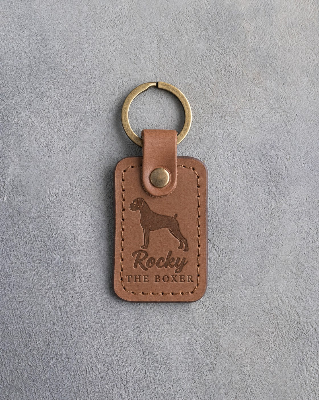 Caramel leather keychain debossed with a Boxer silhouette, the name Rocky and THE BOXER, on gray concrete