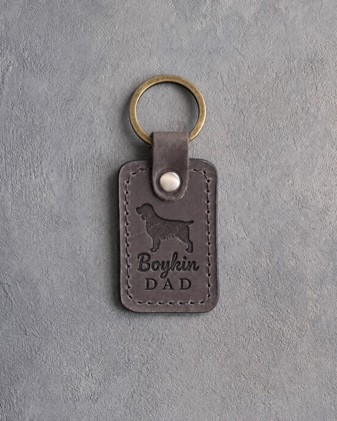 Country gray leather keychain debossed with a Boykin spaniel and Boykin DAD lettering, on gray concrete