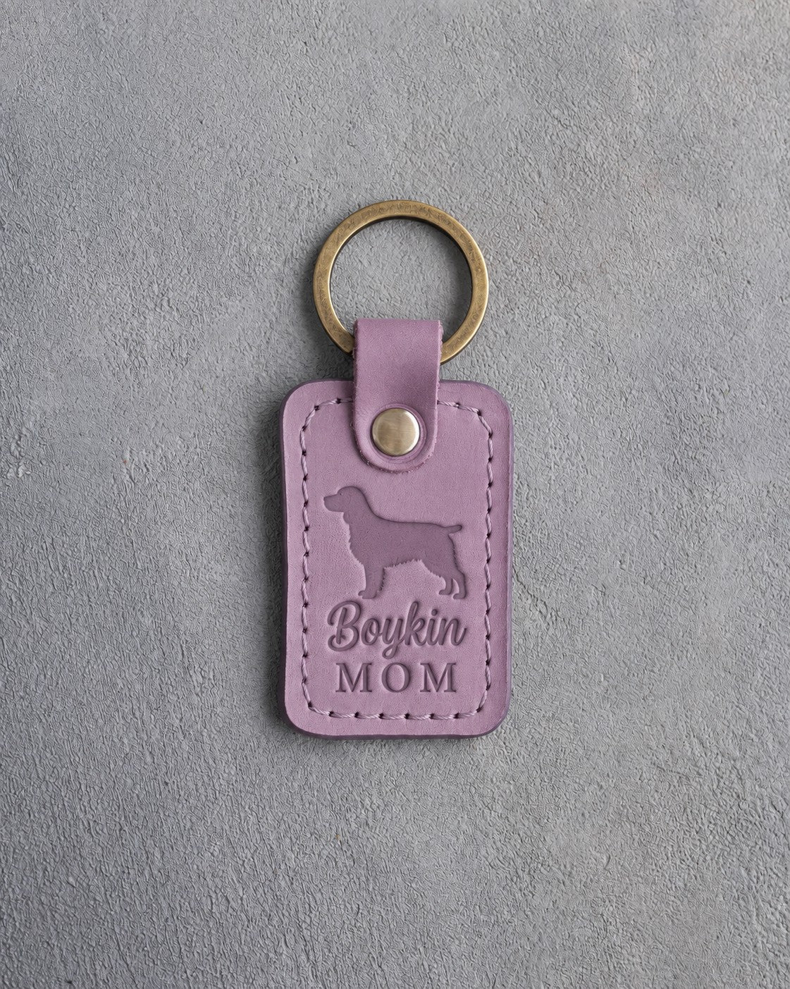 Lilac leather keychain debossed with a Boykin spaniel and the words Boykin MOM, on gray concrete
