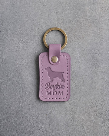 Lilac leather keychain debossed with a Boykin spaniel and the words Boykin MOM, on gray concrete