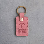 Parisian Blossom pink leather keychain debossed with a Quarter Circle P ranch brand above Brand new and EST 2026, on gray plaster
