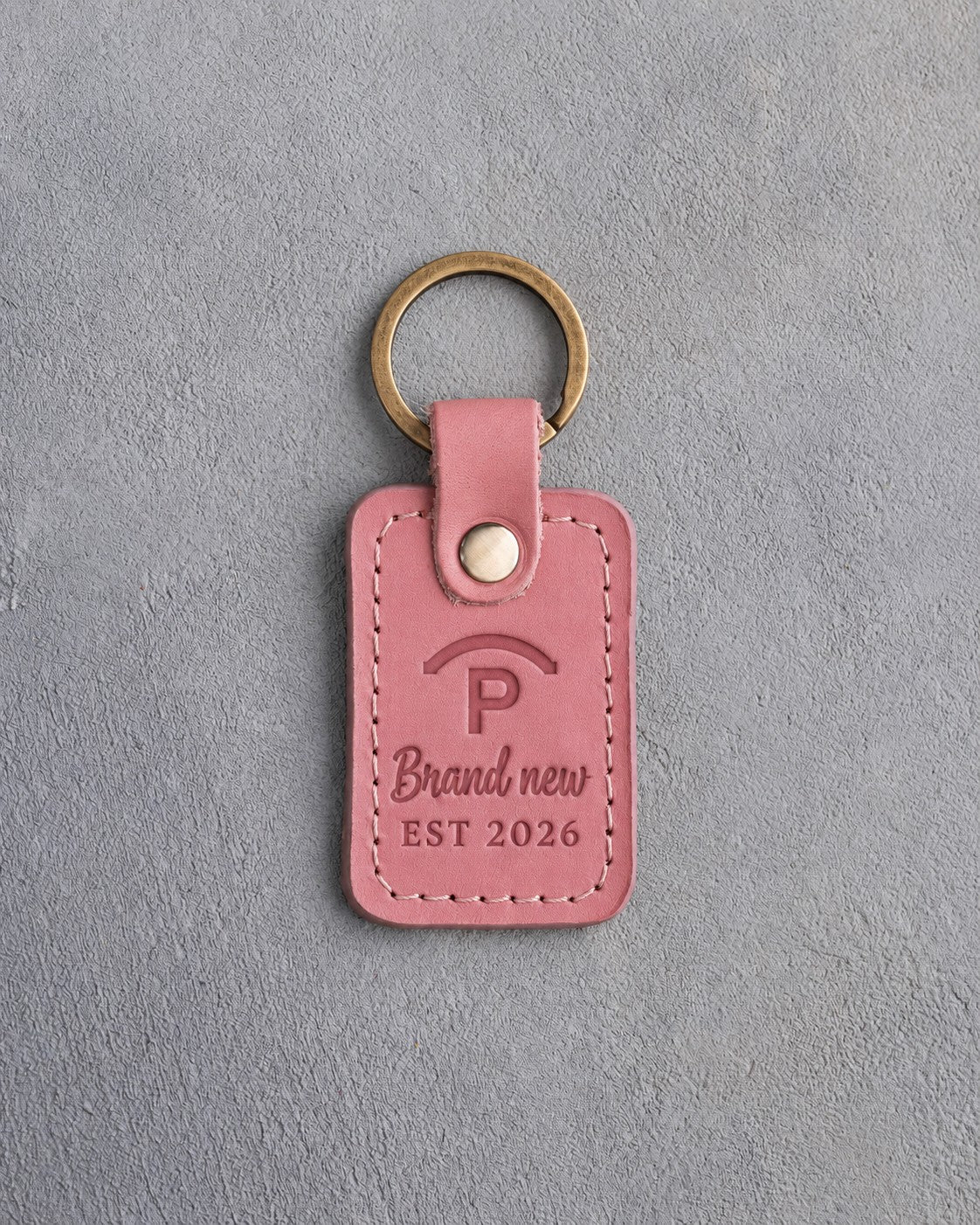 Parisian Blossom pink leather keychain debossed with a Quarter Circle P ranch brand above Brand new and EST 2026, on gray plaster