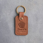 Caramel leather keychain debossed with a fielder's glove and the words Break it in BY SPRING, on gray plaster