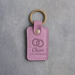 Lilac leather keychain debossed with two interlocked wedding rings above the name Claire and BRIDESMAID, on gray concrete