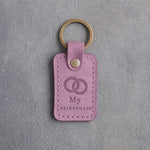 Lilac leather keychain debossed with two interlocked wedding rings above My and BRIDESMAID, on gray concrete
