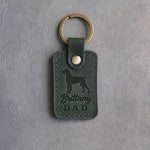 Forest green leather keychain debossed with a Brittany silhouette and the words Brittany DAD, on gray concrete