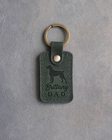 Forest green leather keychain debossed with a Brittany silhouette and the words Brittany DAD, on gray concrete