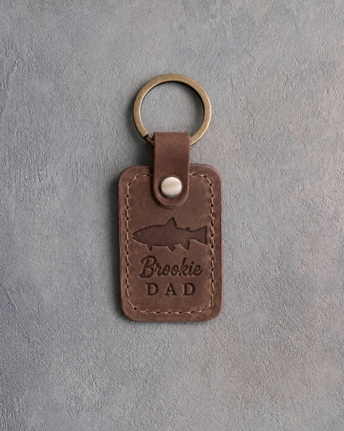 Sicilian brown leather keychain debossed with a brook trout above the words Brookie DAD, on gray plaster