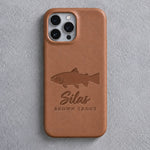 Back of a caramel leather iPhone case debossed with a brown trout above Silas and BROWN TROUT below the camera, on gray plaster