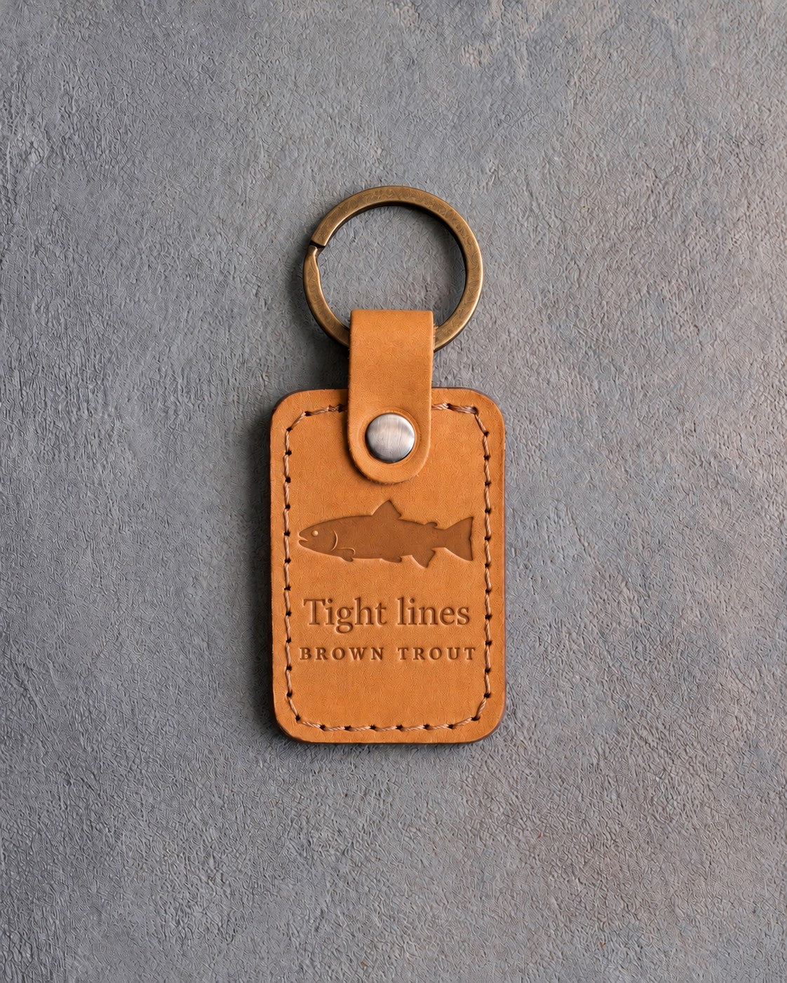 Indian Summer leather keychain debossed with a brown trout above Tight lines and BROWN TROUT, on gray concrete