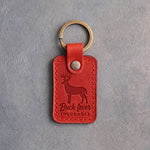 Poppy red leather keychain debossed with a whitetail buck above the words Buck fever INCURABLE, on gray plaster